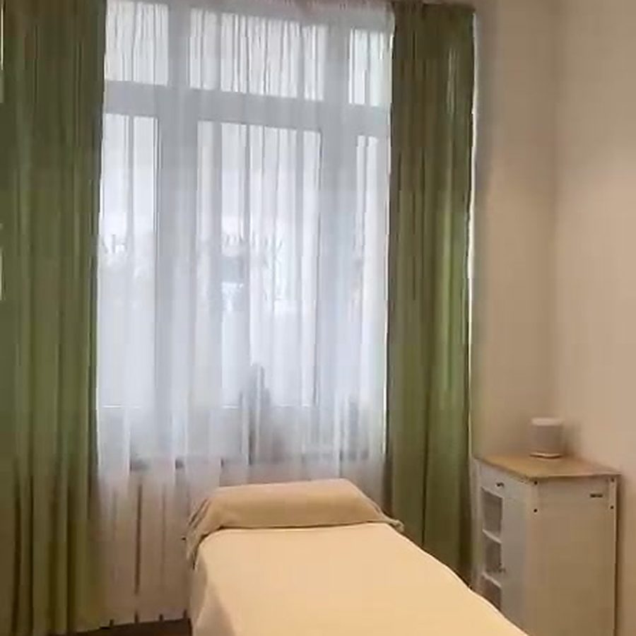 Behandlungsraum mit Liege und grünen Vorhängen